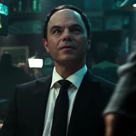 Jed Rees is in his black suit looking at someone.